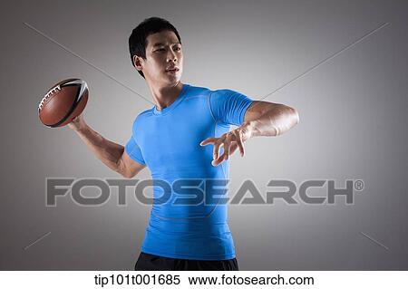 Stock Photography - a fit man in blue shirt about to throw a rugby ball. Fotosearch
