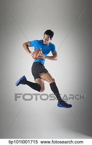 Stock Photography - a fit man in blue shirt jumping with rugby ball. Fotosearch
