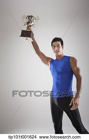 Picture - a fit man in blue shirt posing with trophy. Fotosearch
