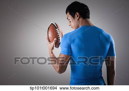 Picture - a fit man in blue shirt posing with rugby ball. Fotosearch
