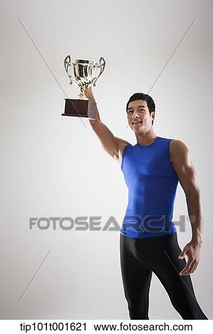 Stock Image - a fit man in blue shirt posing with trophy. Fotosearch