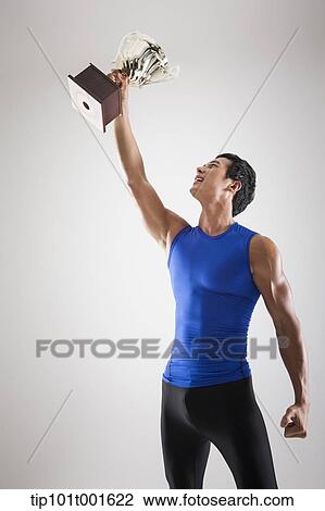Stock Image - a fit man in blue shirt posing with trophy. Fotosearch
