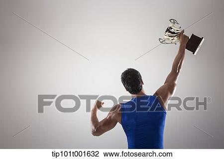 Stock Image - a fit man in blue shirt posing with trophy. Fotosearch