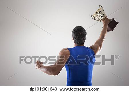 Stock Image - a fit man in blue shirt posing with trophy. Fotosearch