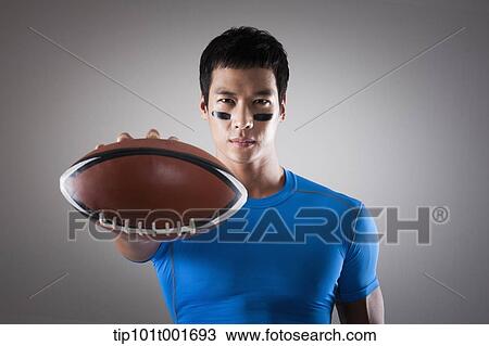 Stock Image - a fit man in blue shirt posing with rugby ball. Fotosearch