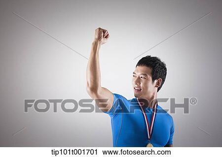 Stock Image - a fit man in blue shirt posing with gold medal around his neck. Fotosearch