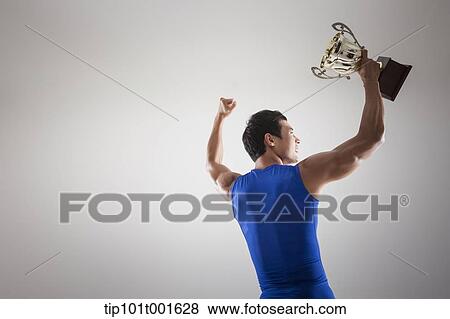 Stock Photo - a fit man in blue shirt posing with trophy. Fotosearch