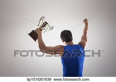 Stock Photo - a fit man in blue shirt posing with trophy. Fotosearch