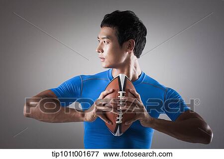 Stock Photo - a fit man in blue shirt posing with rugby ball. Fotosearch
