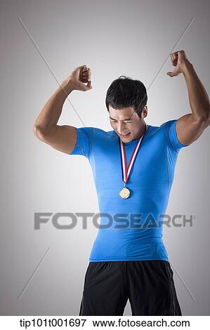 Stock Photo - a fit man in blue shirt posing with gold medal around his neck. Fotosearch