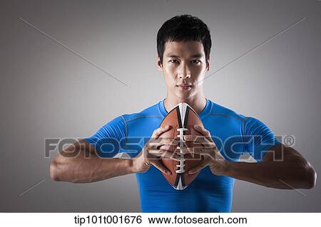 Stock Photograph - a fit man in blue shirt posing with rugby ball. Fotosearch