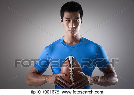 Stock Photography - a fit man in blue shirt posing with rugby ball. Fotosearch