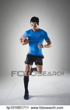 a fit man in blue shirt running with rugby ball View Large Photo Image Stock Image - a fit man in blue shirt running with rugby ball. Fotosearch