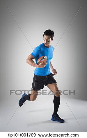 a fit man in blue shirt running with rugby ball View Large Photo Image Stock Photo - a fit man in blue shirt running with rugby ball. Fotosearch