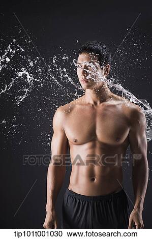 Stock Image - a fit man posing in black background with water splash. Fotosearch