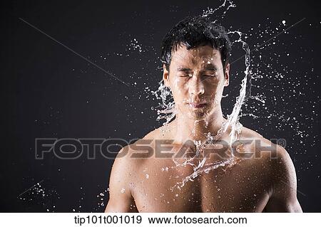 Stock Photo - a fit man posing in black background with water splash. Fotosearch