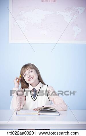 Stock Image - a girl dressed as a student sitting at a desk with a book. Fotosearch