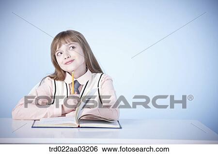 a girl dressed as a student sitting at a desk with a book View Large Photo Image Stock Photograph - a girl dressed as a student sitting at a desk with a book. Fotosearch