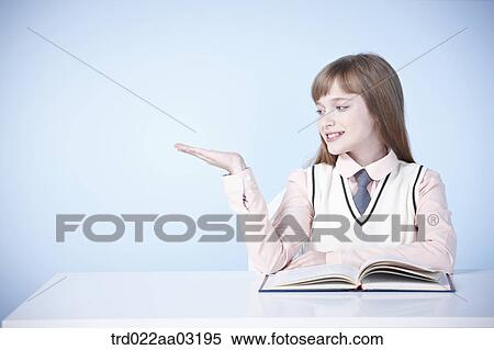 a girl dressed as a student sitting at a desk with a book View Large Photo Image Stock Photography - a girl dressed as a student sitting at a desk with a book. Fotosearch