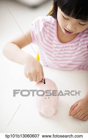 Stock Photo - a girl putting money into piggy bank. Fotosearch