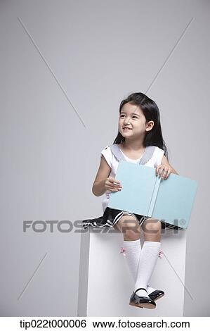 Stock Photograph - a girl sitting on a box with a book. Fotosearch