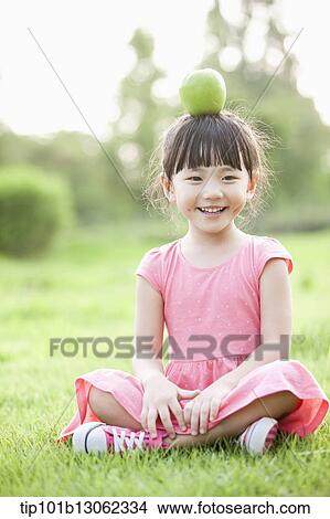 Picture - a girl sitting on grass playing with fruits. Fotosearch