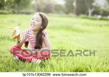 Stock Photo - a girl sitting on the grass eating a banana. Fotosearch