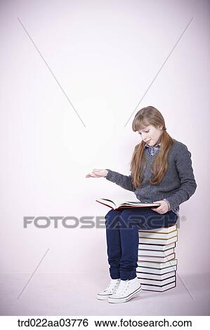 a girl with a book sitting on a pile of books View Large Photo Image Stock Photograph - a girl with a book sitting on a pile of books. Fotosearch