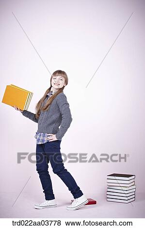 a girl with a book standing next to a pile of books View Large Photo Image Stock Photo - a girl with a book standing next to a pile of books. Fotosearch