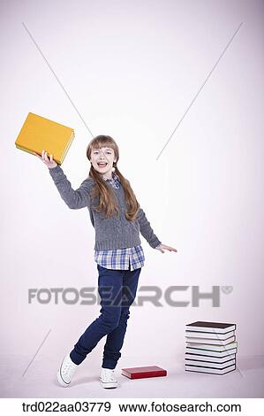 a girl with a book standing next to a pile of books View Large Photo Image Stock Photo - a girl with a book standing next to a pile of books. Fotosearch