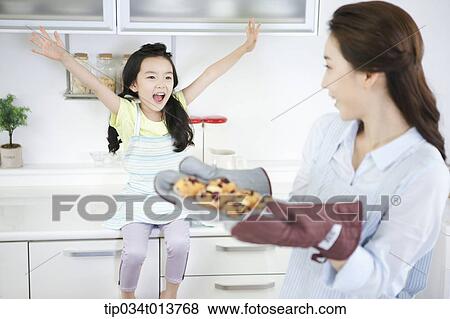 Stock Photo - a happy daughter looking at mother with cookies. Fotosearch