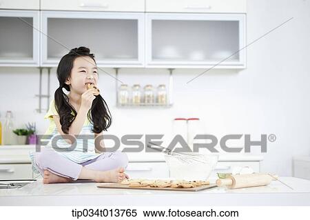 Stock Photography - a kid sitting on kitchen table eating a cookie. Fotosearch