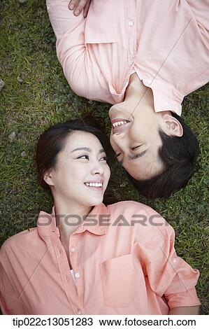 Stock Image - a man and a woman lying on a grass field. Fotosearch