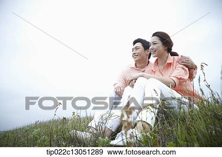 Stock Photo - a man and a woman sitting on a grass field. Fotosearch