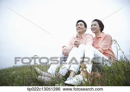 Stock Photograph - a man and a woman sitting on a grass field. Fotosearch