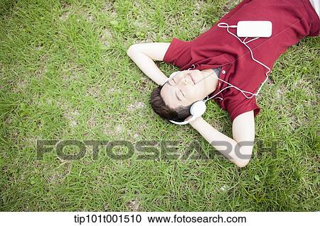 Stock Image - a man lying on the grass listening to music. Fotosearch