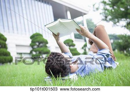 Stock Image - a man lying on the grass reading a book. Fotosearch