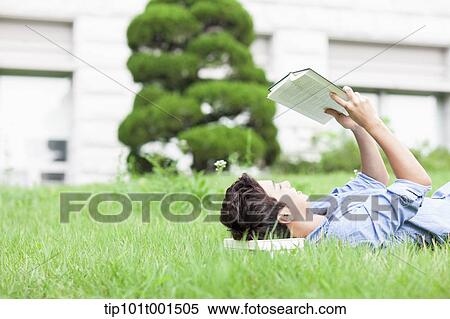 Stock Photography - a man lying on the grass reading a book. Fotosearch