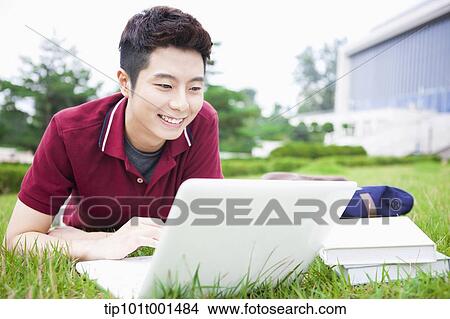 Picture - a man lying on the grass using laptop. Fotosearch