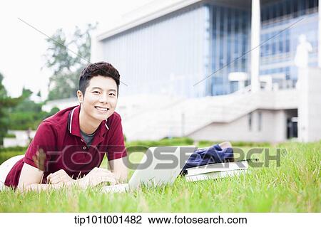 Stock Image - a man lying on the grass using laptop. Fotosearch