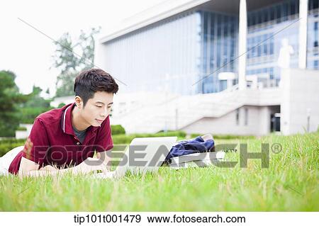 Stock Photo - a man lying on the grass using laptop. Fotosearch