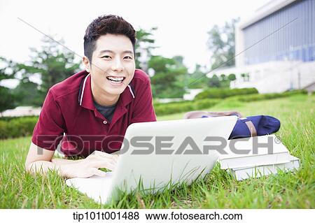 Stock Photo - a man lying on the grass using laptop. Fotosearch