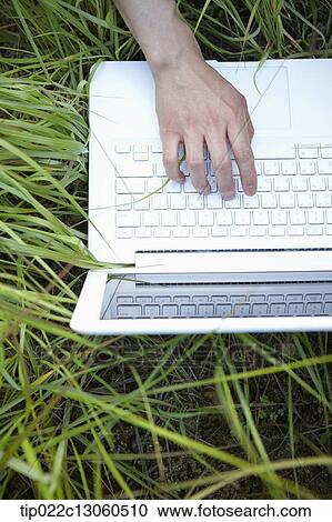 Stock Image - a man lying on the grass working with laptop. Fotosearch