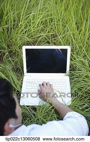 Stock Photo - a man lying on the grass working with laptop. Fotosearch