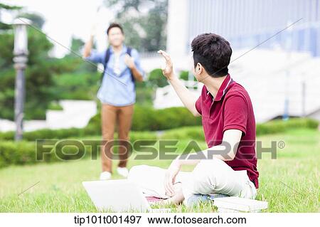 Stock Photo - a man sitting on the grass greeting a friend. Fotosearch