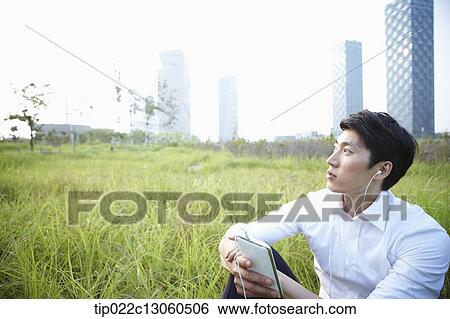 a man sitting on the grass listening to music View Large Photo Image Stock Photograph - a man sitting on the grass listening to music. Fotosearch
