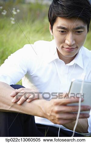 Stock Photography - a man sitting on the grass listening to music. Fotosearch