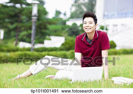 Stock Image - a man sitting on the grass using laptop. Fotosearch