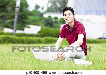 Stock Photography - a man sitting on the grass using laptop. Fotosearch