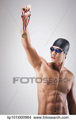 Picture - a man with swimming goggle and hat holding a golden medal. Fotosearch